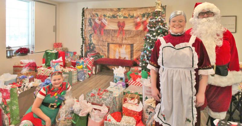 Left to right, Santa’s elf (Emery Williams), Mrs. Claus and Santa (Ashlynn and Joey Passarelli) showcase the 93 gifts they will give to the senior residents of Surrey Hills Estates, 11300 Surrey Hills Boulevard in Yukon, during the Dec. 18 Christmas celebration. Photo / Carol Mowdy Bond