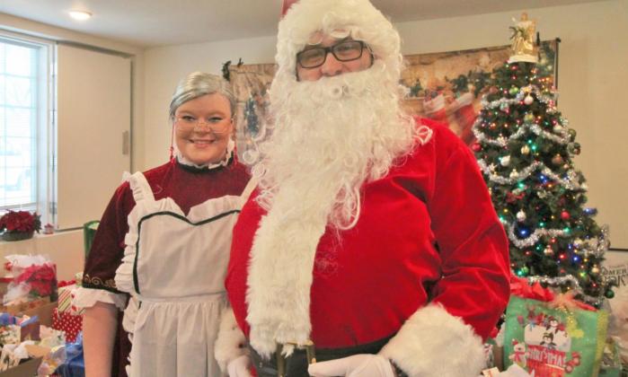 Mrs. Claus and Santa (Ashlynn and Joey Passarelli) stand in front of the 93 gifts they will give to the senior residents of Surrey Hills Estates, 11300 Surrey Hills Boulevard in Yukon, during the Dec. 18 Christmas celebration.